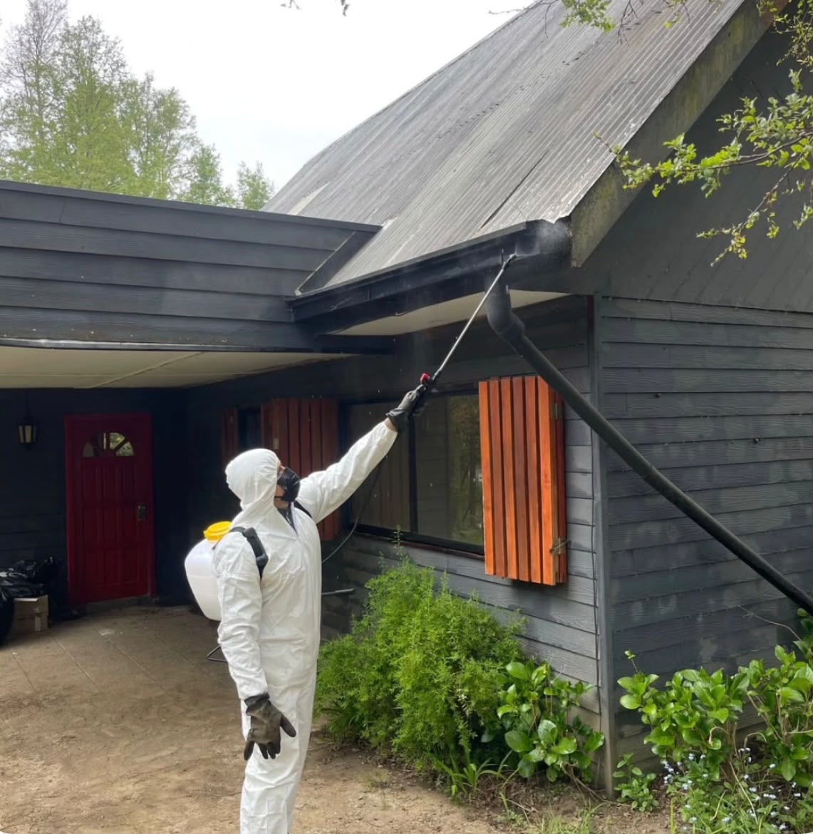 Técnico de FumiDefense con equipo de protección completo aplicando fumigación profesional en el exterior de una cabaña en Pucón